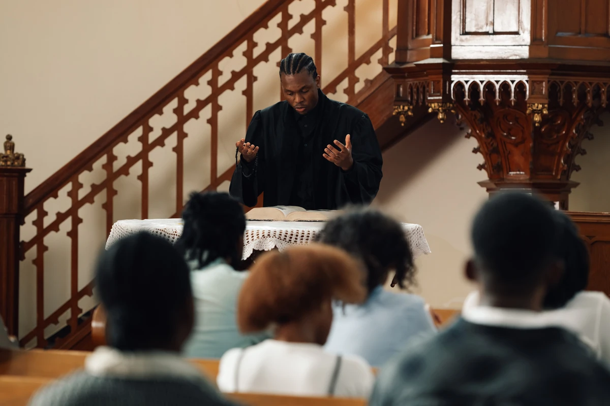 Older man in a suit reading from an open book near a menorah.