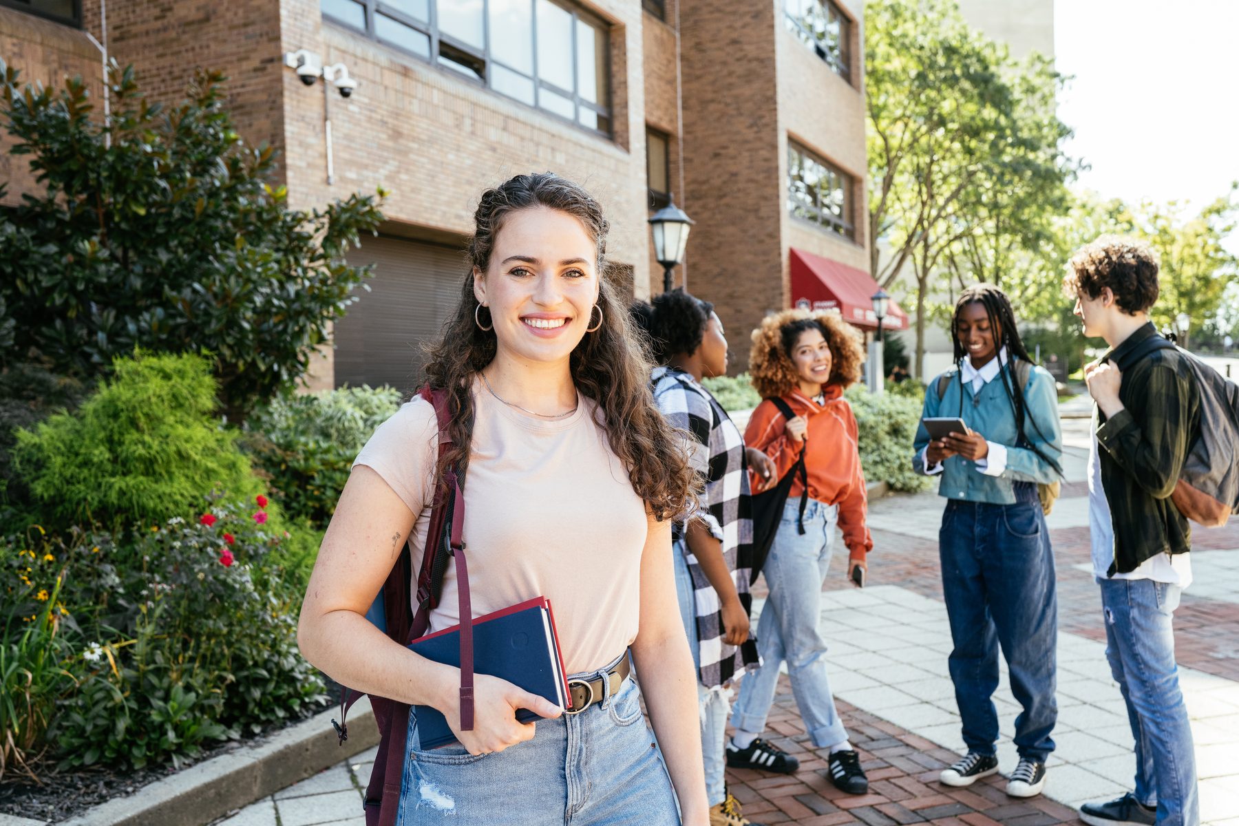 Woman in the foreground smiling toward the camera, holding a notebook, with fellow students nearby.
